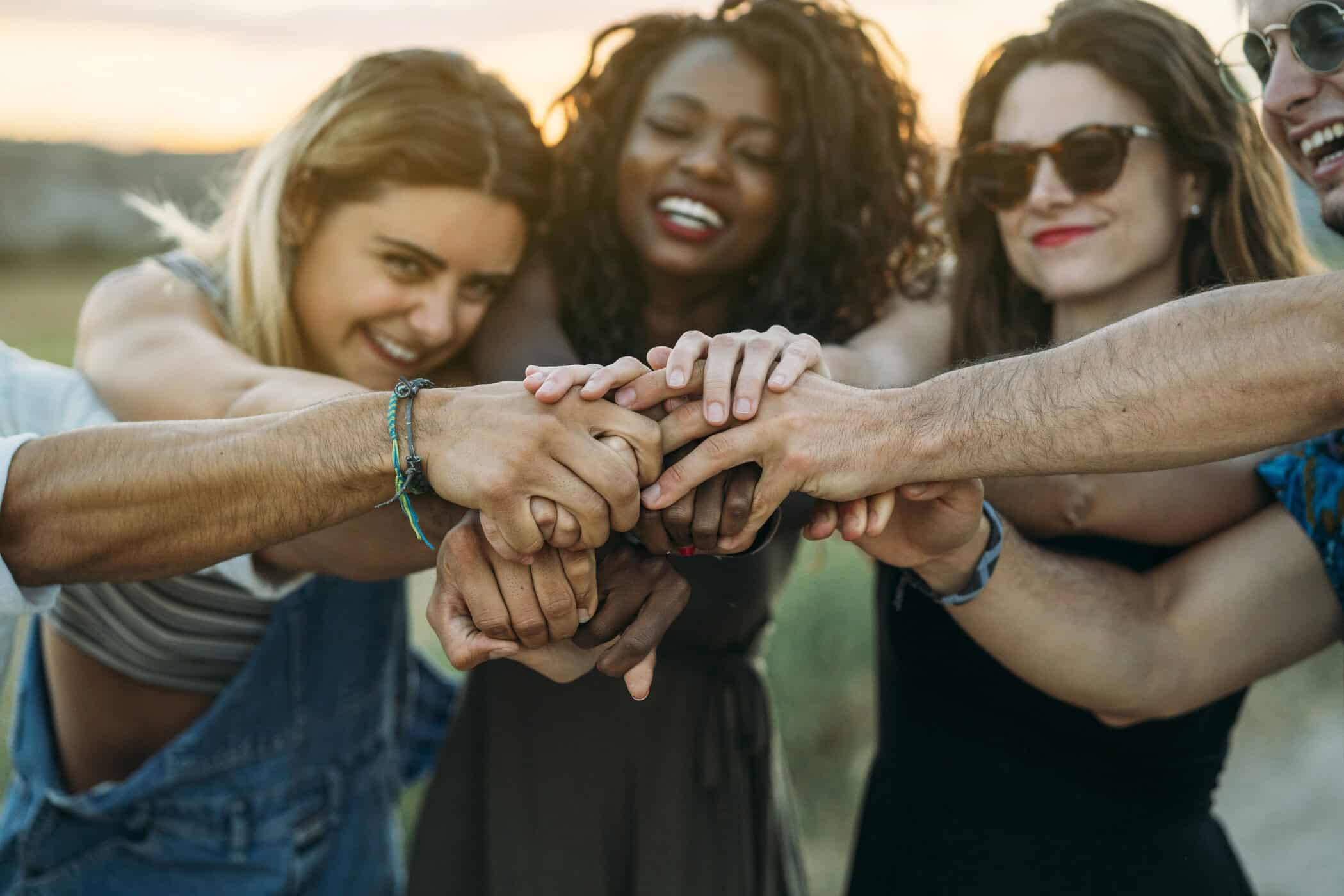 Gruppe von fünf lachenden Freund:innen hält im Freien die Hände zusammen symbolisiert Freundschaft und ADHS.
