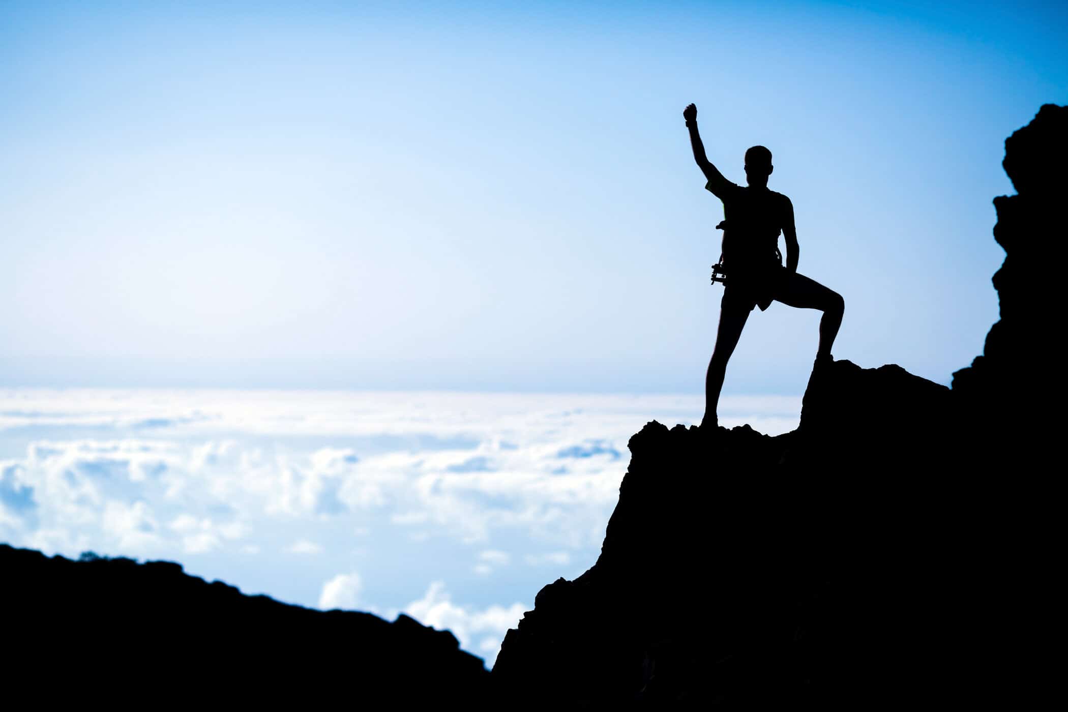 Silhouette einer Person auf einem Berggipfel über den Wolken – Sinnbild für Klarheit, Motivation und neue Perspektiven bei ADHS und Dopamin.