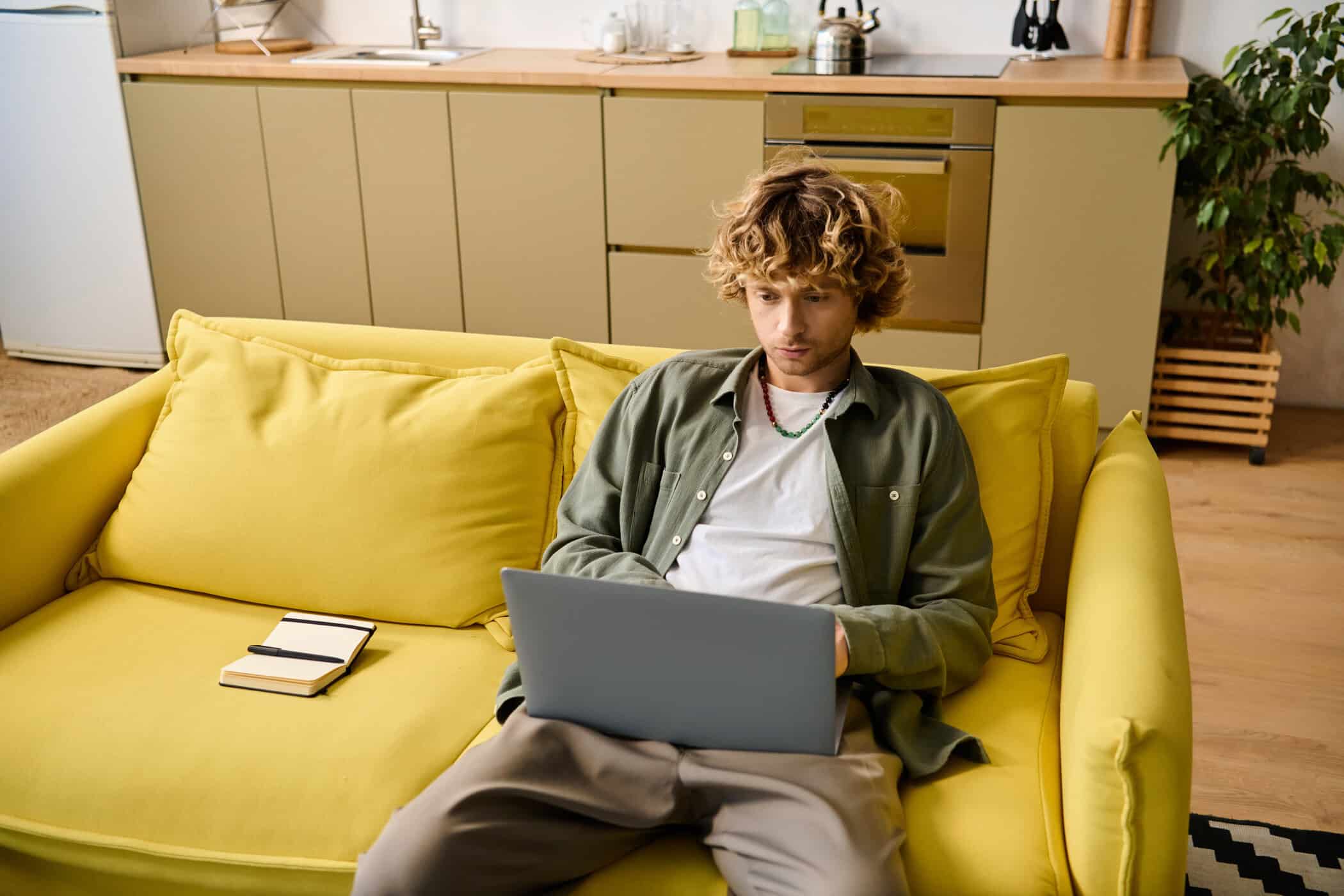 Junger Erwachsener sitzt mit Laptop auf einem Sofa zu Hause und nimmt an einer Teletherapie per Videogespräch teil.