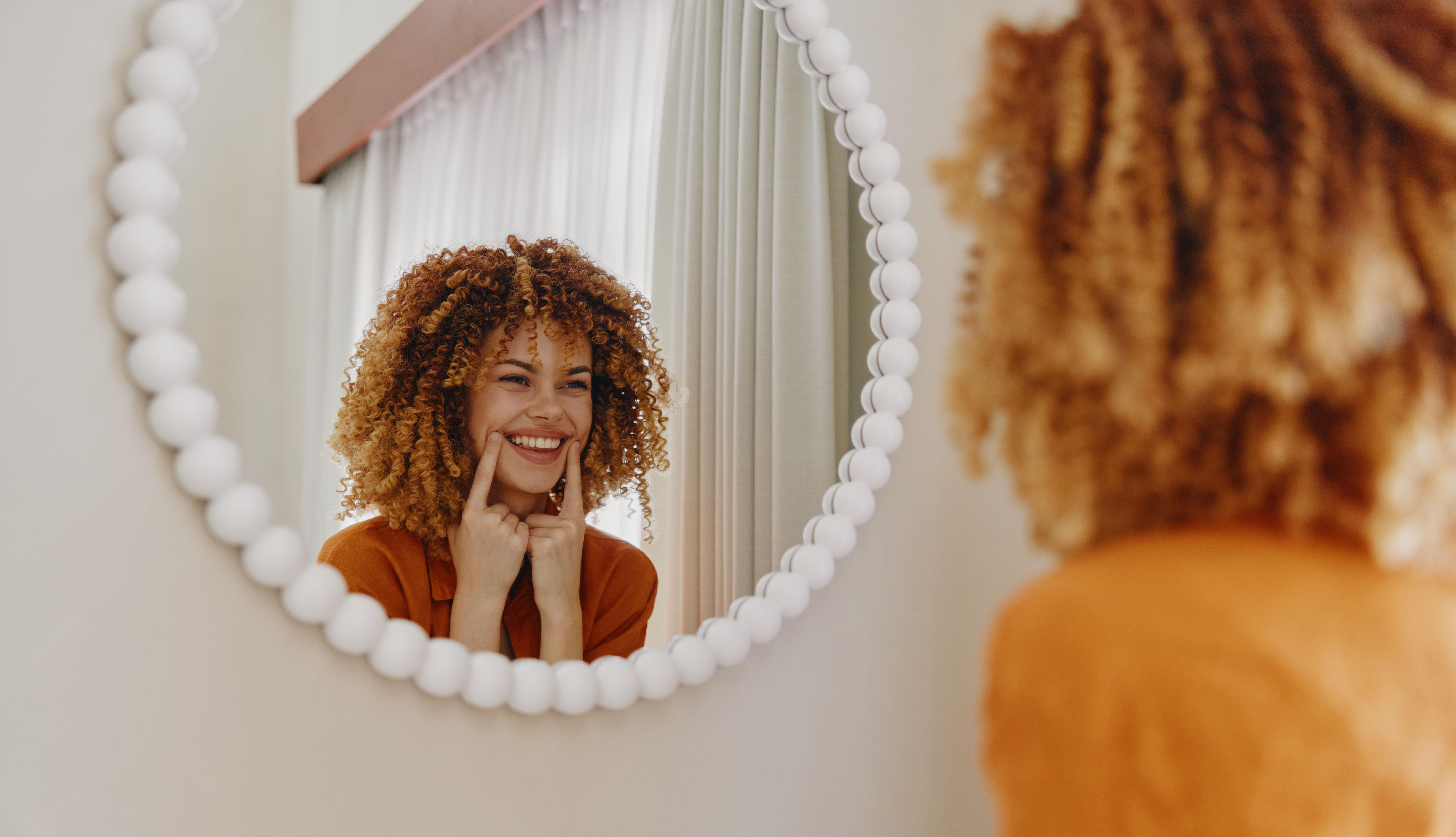 Junge Frau lächelt sich im Spiegel an – symbolisches Bild für Selbstwahrnehmung und emotionale Regulation trotz ADHS im Erwachsenenalter.