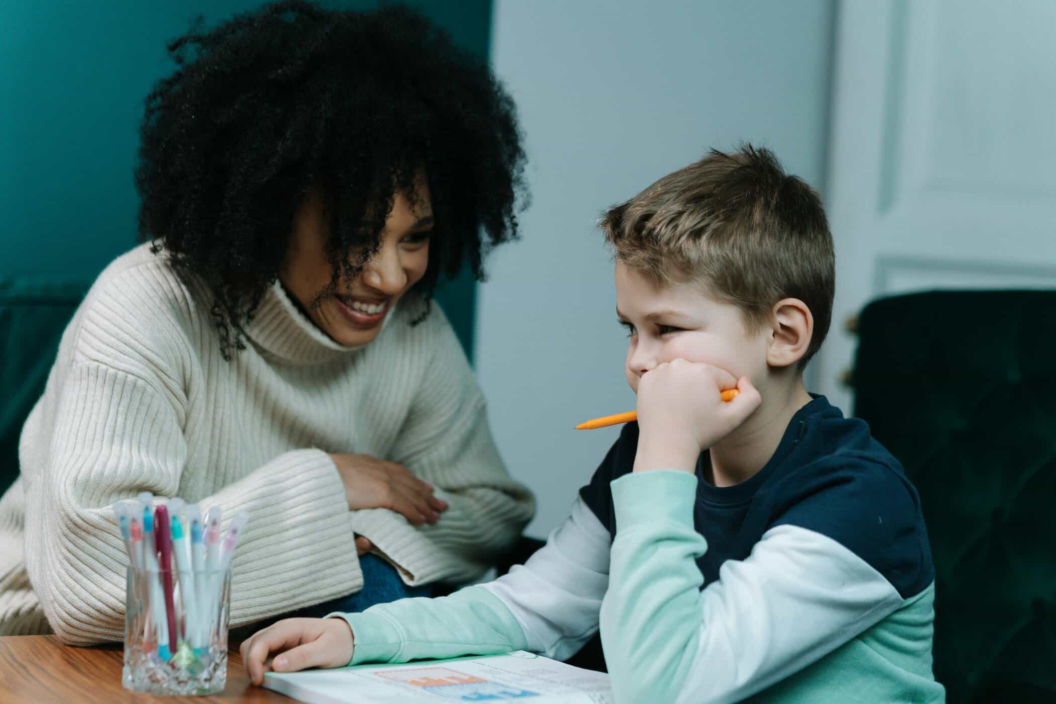 Junge guckt frustriert auf Hausaufgaben und wird von einer Frau motivierend angeguckt
