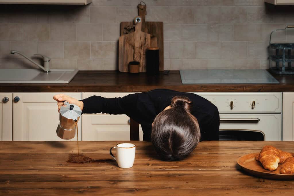Erschöpfte Frau verfehlt beim Einschenken die Kaffeetasse und zeigt den Koffein-Crash, den Koffein und ADHS gemeinsam auslösen können.