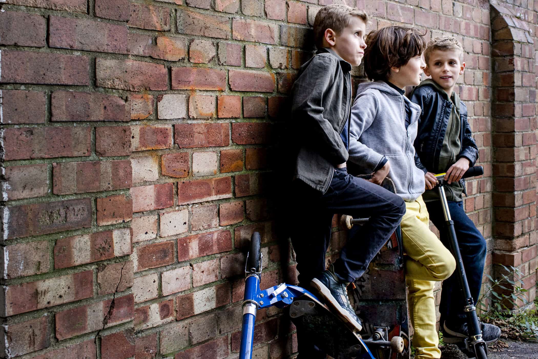 Drei Jungen mit Fahrrad und Roller an einer Backsteinmauer – Alltag mit ADHS bei Jungen.