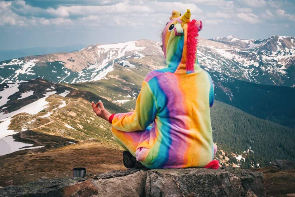 Person im bunten Einhorn-Kostüm meditiert auf einem Berggipfel – Symbolbild für kreatives Problemlösen bei ADHS