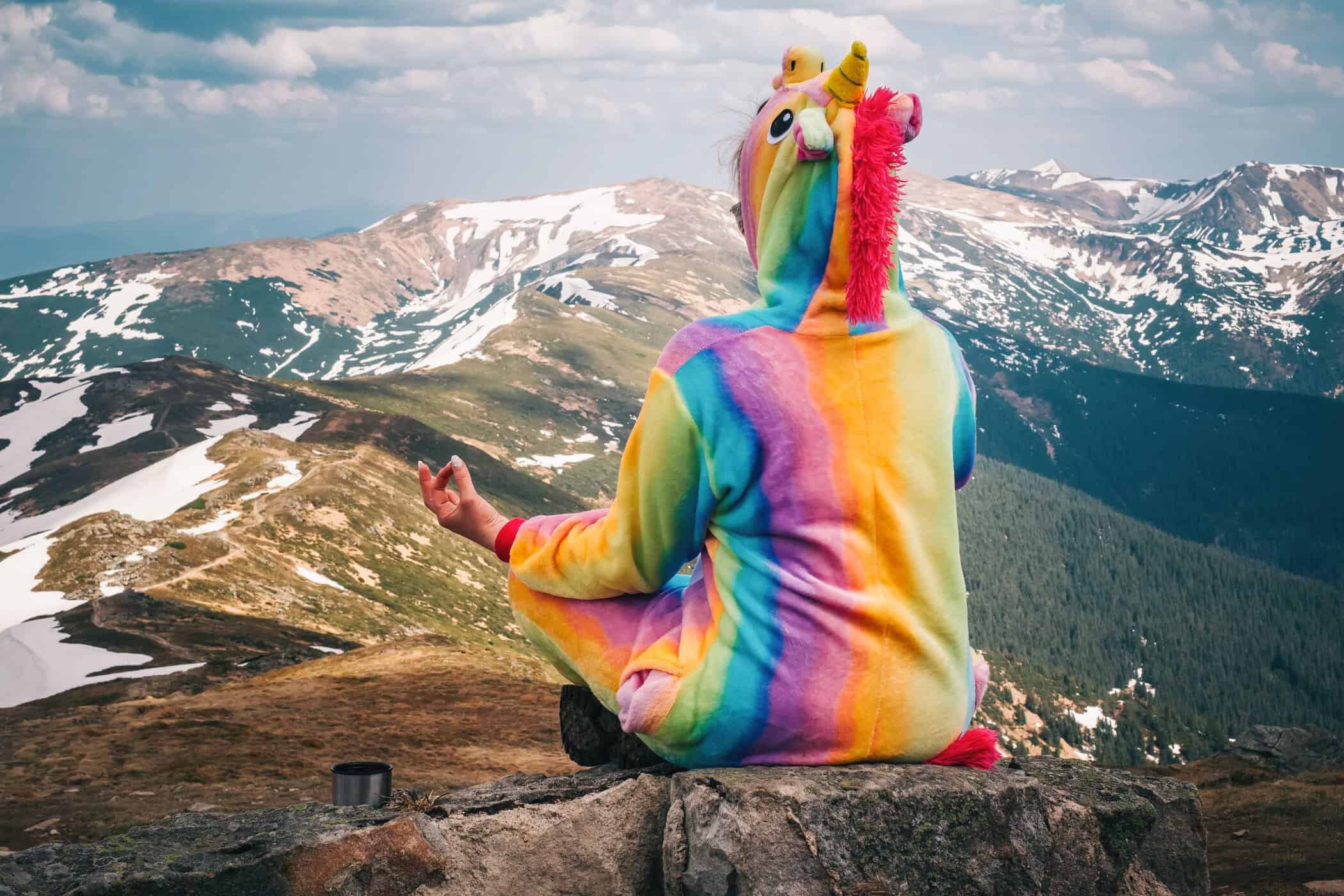 Person im bunten Einhorn-Kost&uuml;m meditiert auf einem Berggipfel &ndash; Symbolbild f&uuml;r kreatives Probleml&ouml;sen bei ADHS