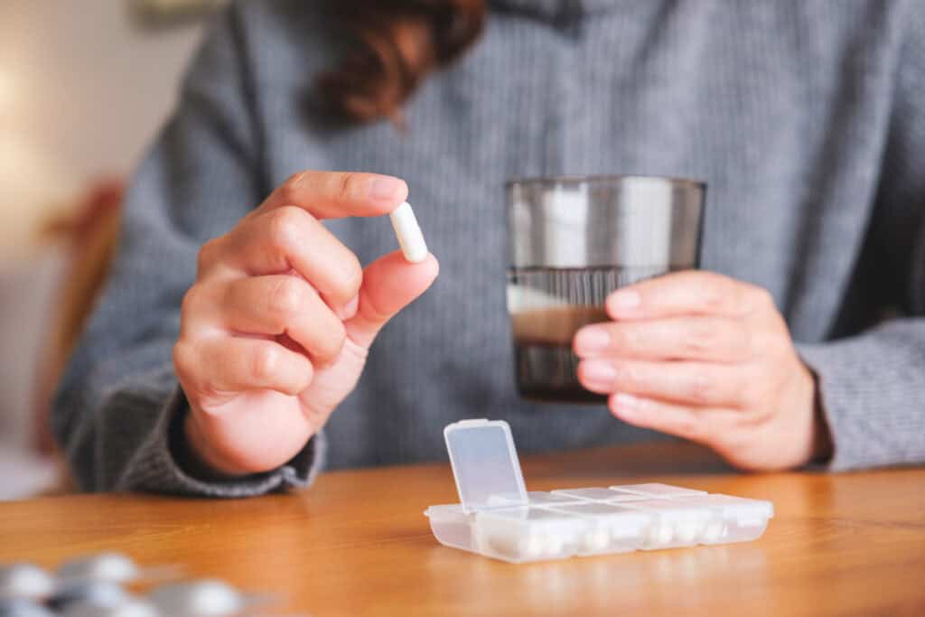 Person hält eine Tablette über einer geöffneten Pillenbox, daneben ein Glas Wasser – sinnbildlich für die tägliche Einnahme und die Medikinet Erfahrungen Betroffener im Alltag