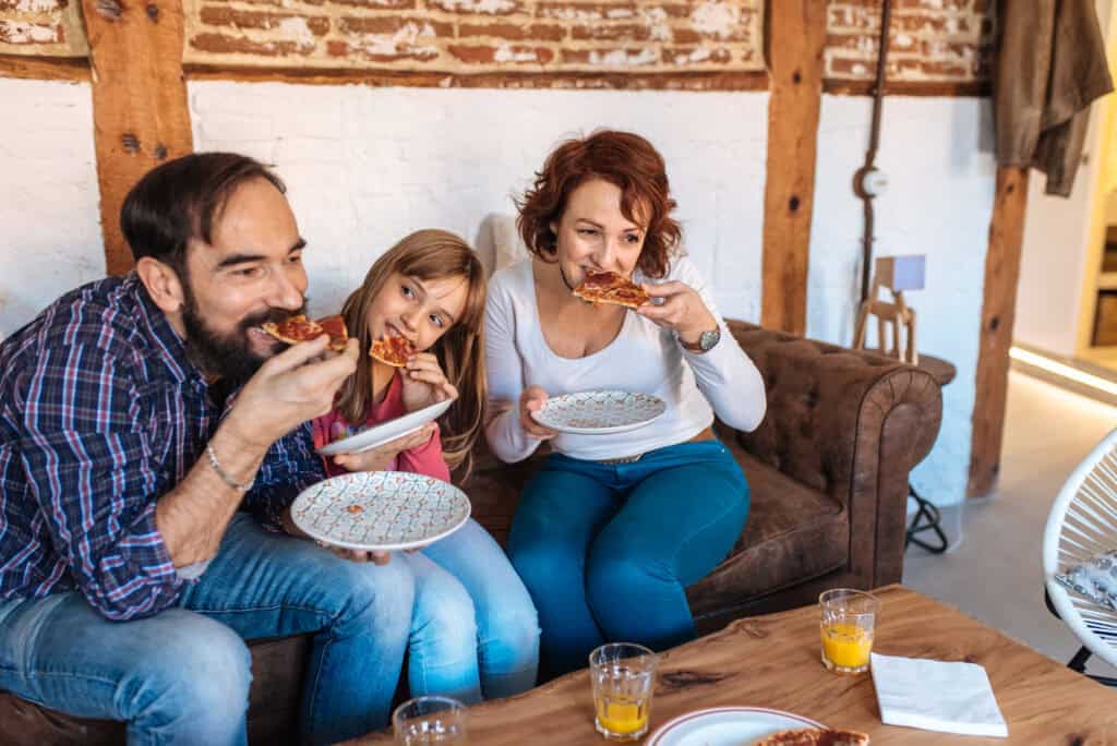 Familie mit Kind isst gemeinsam Pizza auf dem Sofa – Symbolbild für ADHS und Familie im Alltag