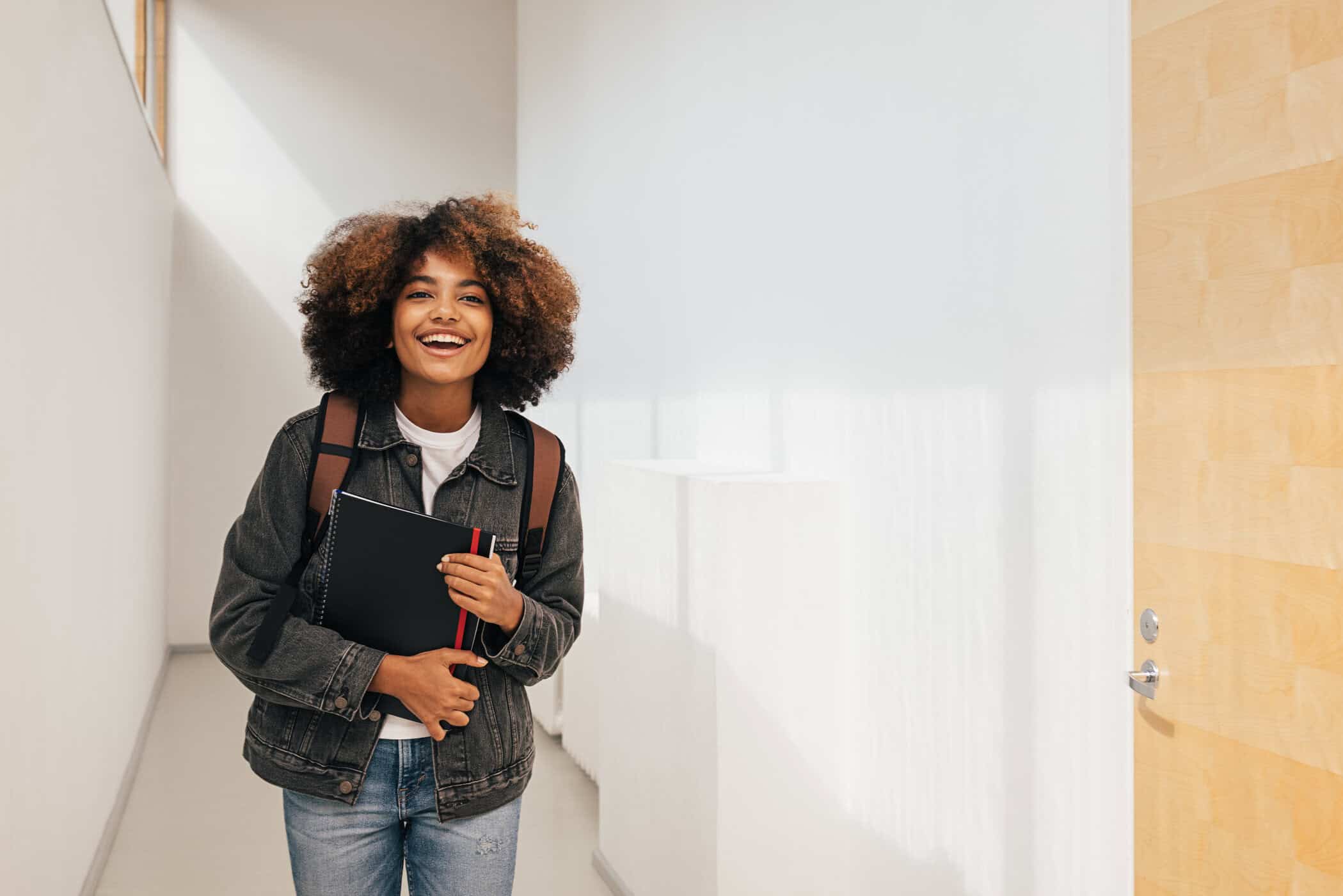 L&auml;chelnde Studentin mit Rucksack und Notizblock im Flur symbolisiert gelingendes studieren mit ADHS.
