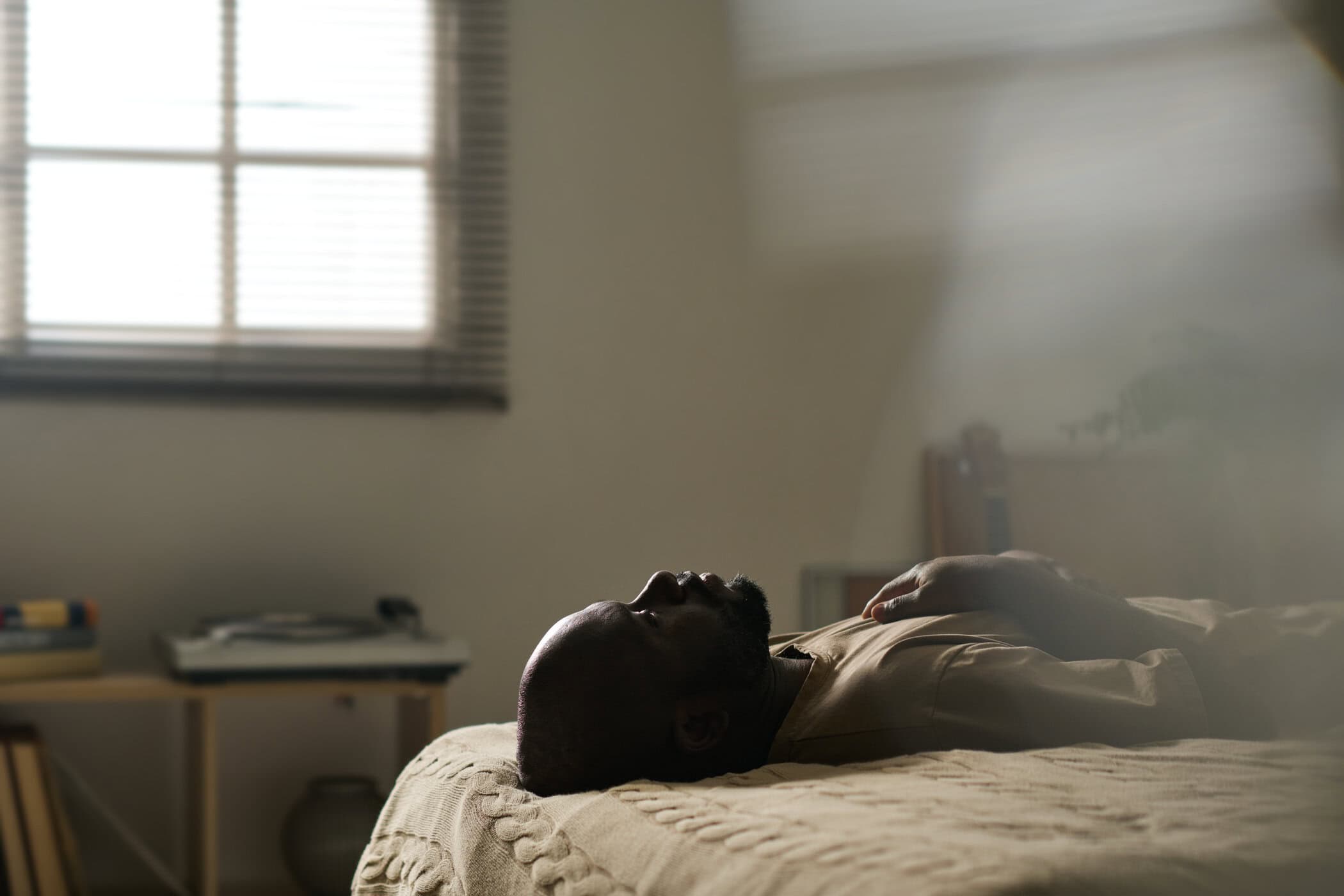 Mann liegt schlaflos auf seinem Bett, w&auml;hrend die Sonne aufgeht - symbolisiert Panikattacke Nachts