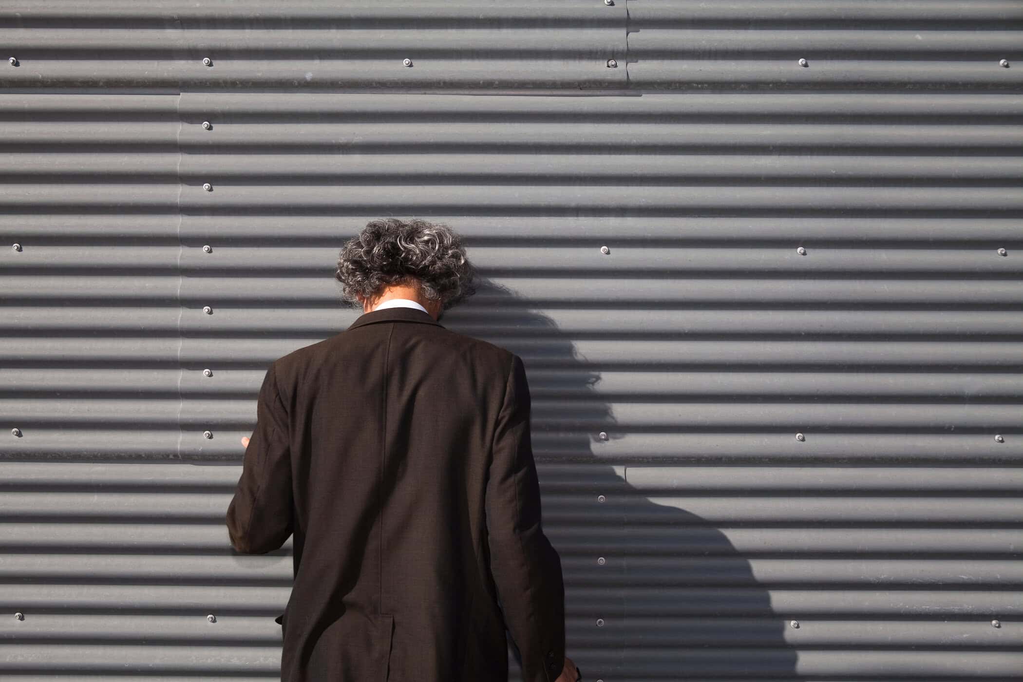 Person lehnt ersch&ouml;pft den Kopf an eine Wand - symbolisiert Shutdown bei Autismus als Zustand des R&uuml;ckzugs und der &Uuml;berforderung.
