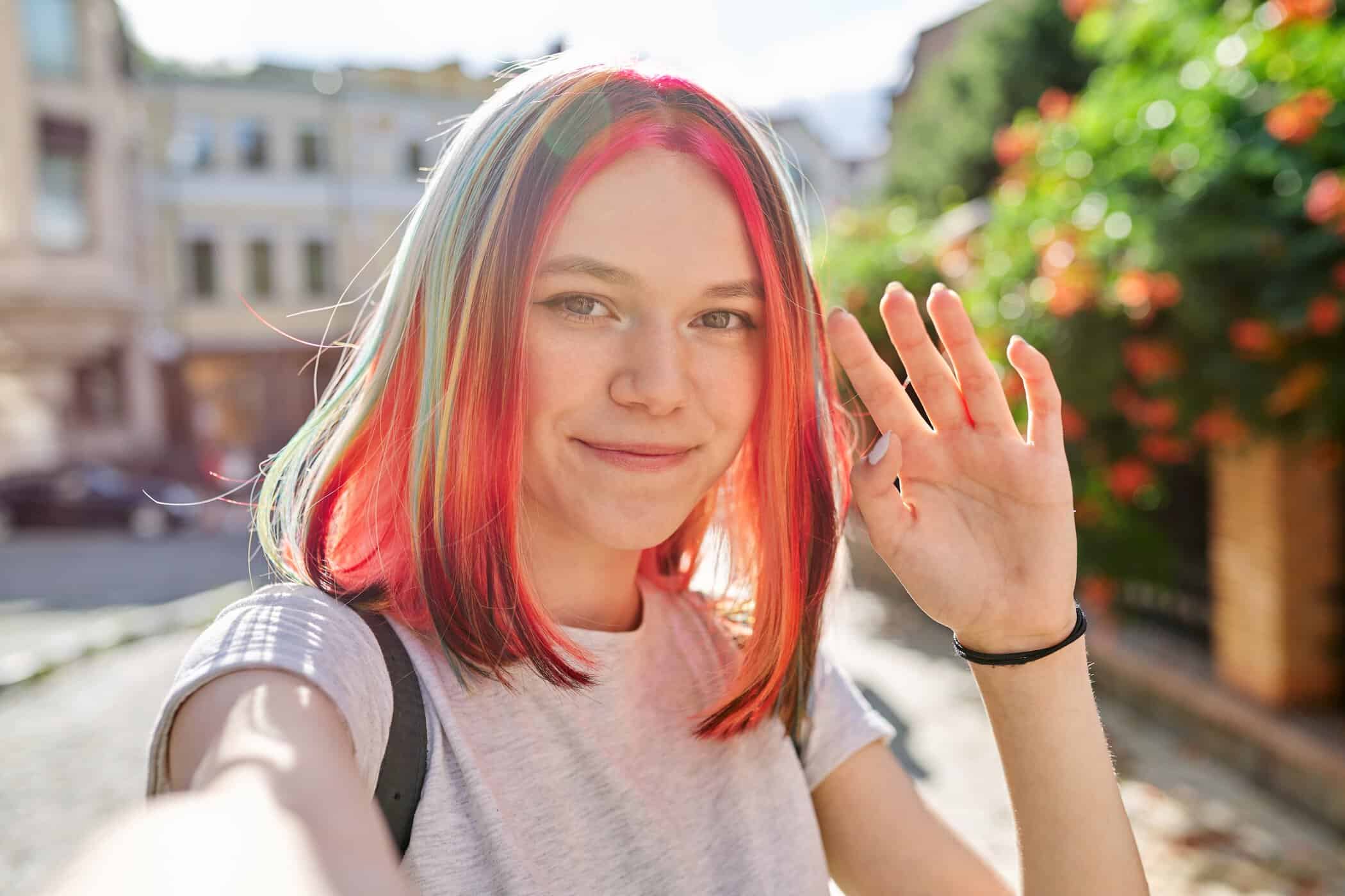 Jugendliche mit bunten Haaren winkt in die Kamera – Sinnbild für Autismus und Pubertät
