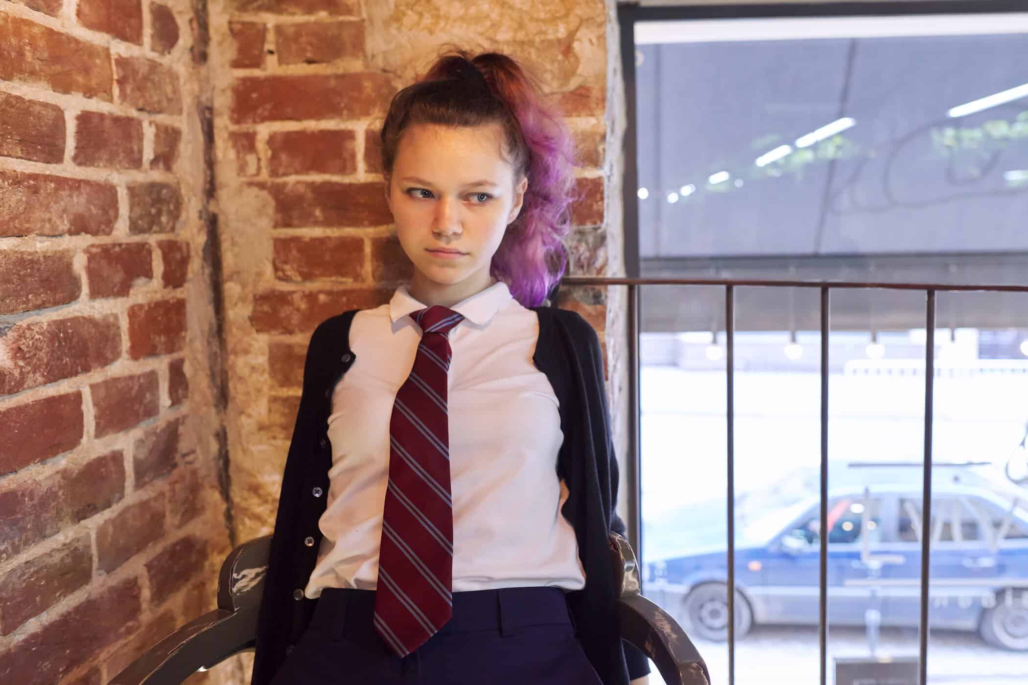 Junges Mädchen in Schuluniform guckt kritisch, symbolisiert Autismus und Pubertät