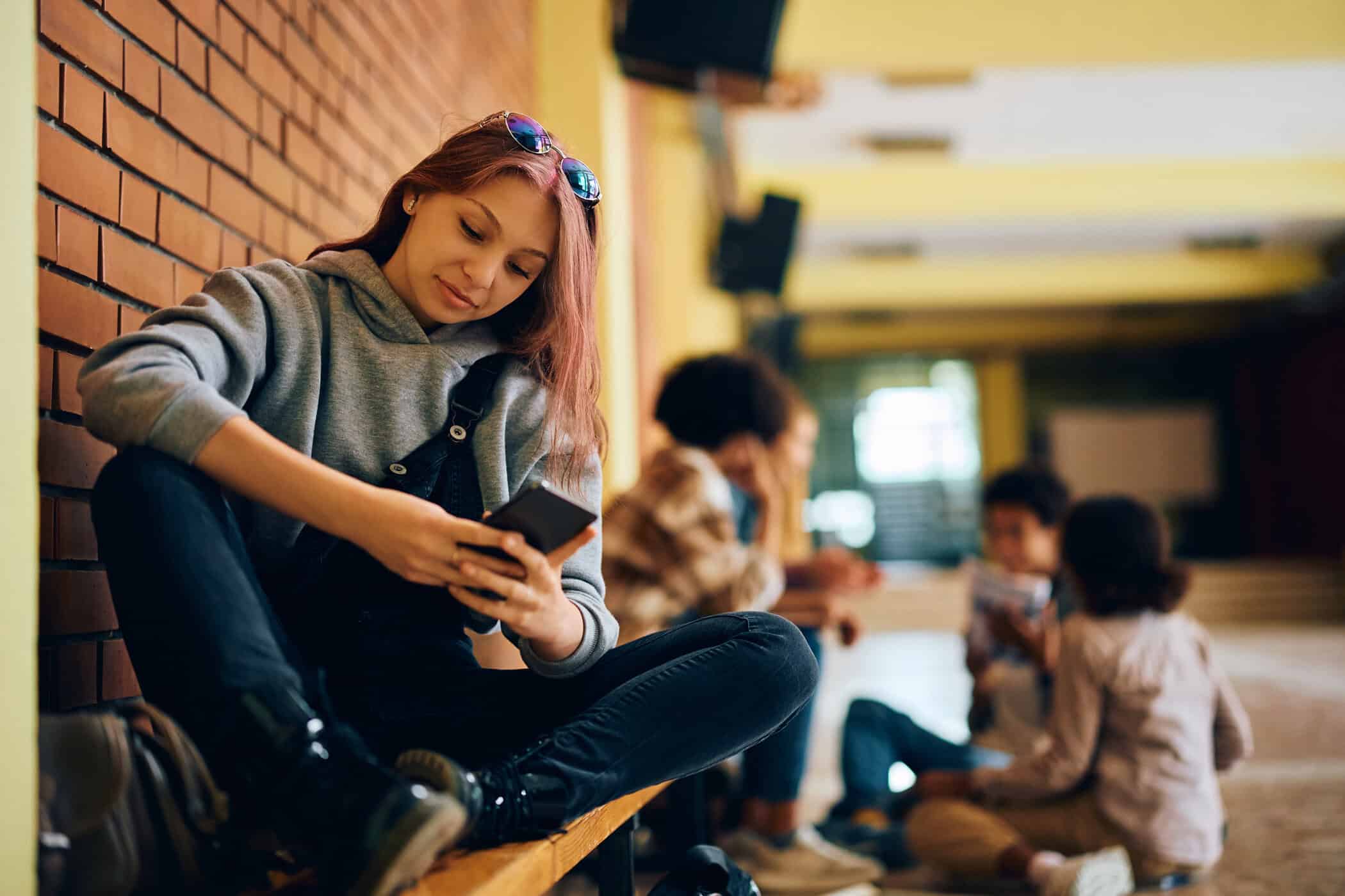 Mädchen guckt verträumt auf ihr Handy, symbolisiert Autismus und Pubertät